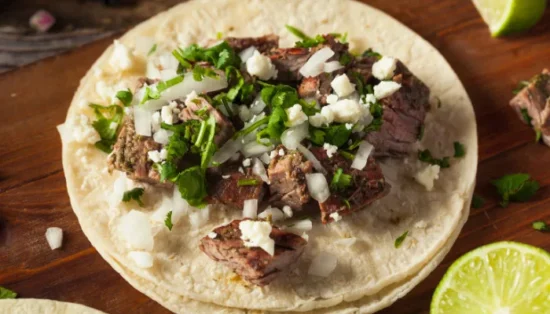 Freshly prepared beef carnitas street tacos topped with diced white onion, cilantro, and lime wedge on corn tortillas for wholesale food service.