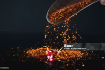 Vibrant chili flakes and dried peppers showcase culinary artistry against a dark background.