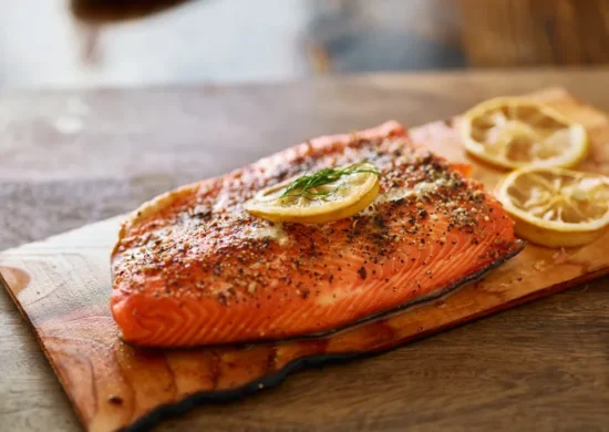 Perfectly cooked cedar-planked salmon garnished with caramelized lemon and fresh dill on a rustic board.