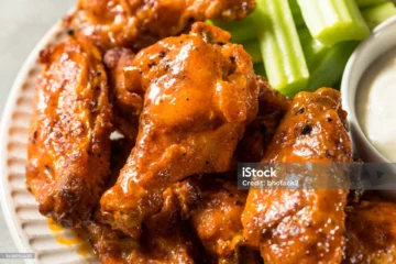Crispy chicken wings with sauce, celery sticks, and dipping sauce for a perfect shareable snack.
