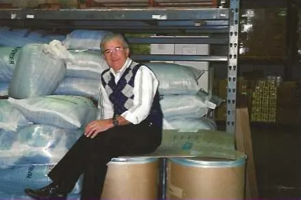 Professional in wholesale food distribution warehouse standing beside large bulk storage drums and packaged goods on shelves.