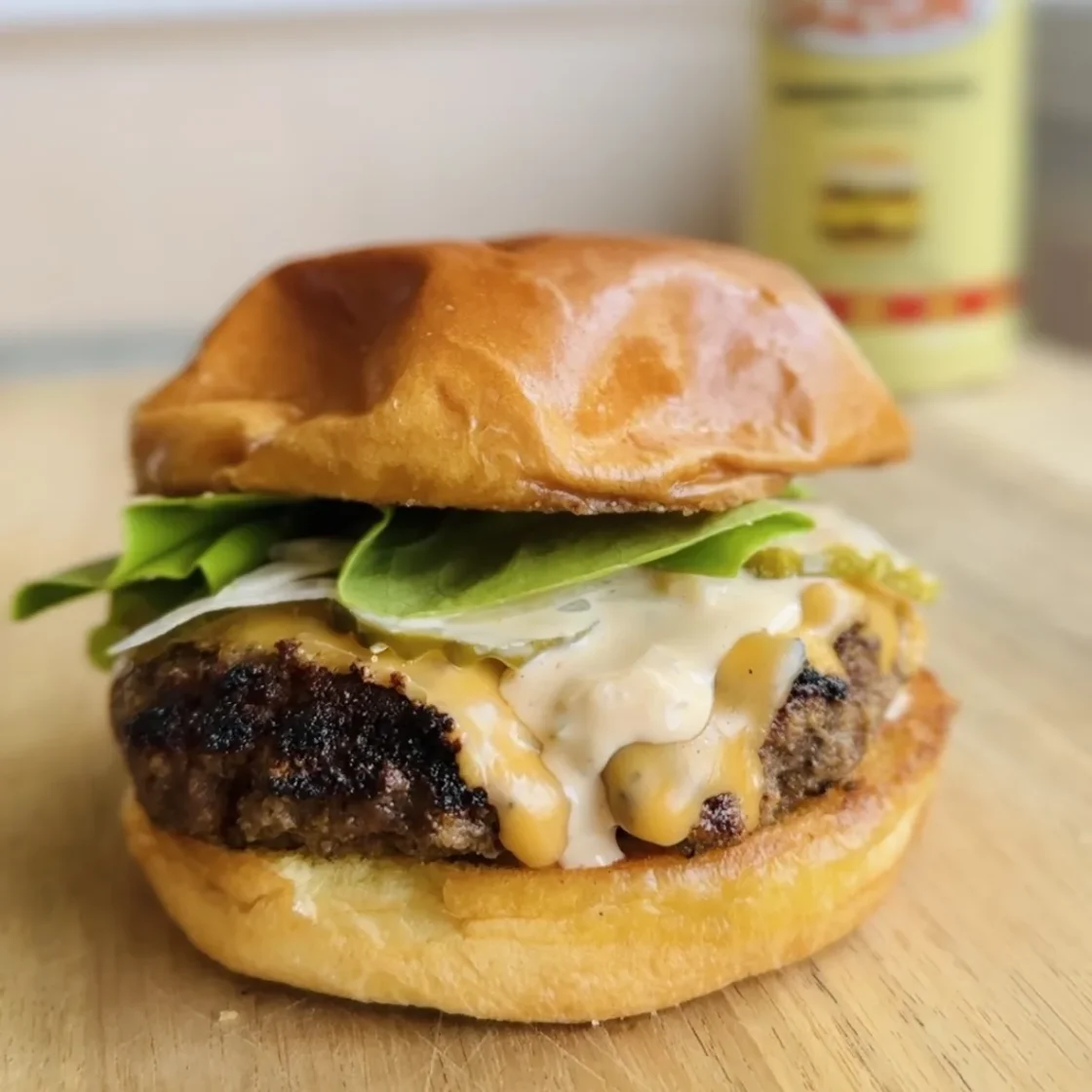 Premium beef burger patty topped with melted cheese, creamy sauce, and fresh arugula on toasted brioche bun for foodservice distribution.