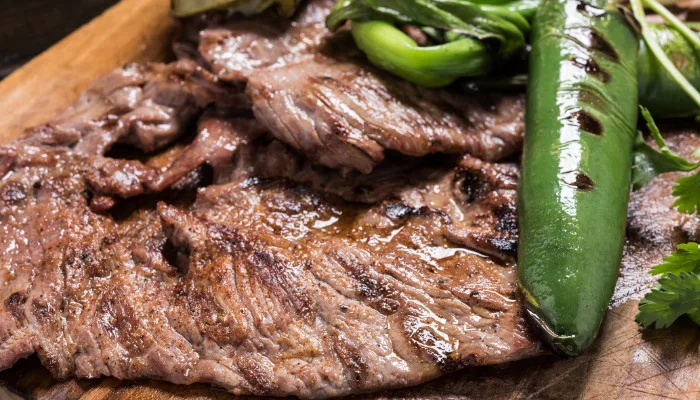 Sliced grilled beef steak with char marks served alongside fresh green peas and vegetables on wooden board, ideal for foodservice and wholesale distribution.
