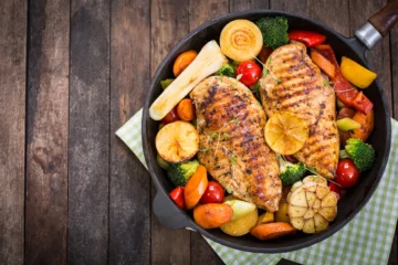 Grilled chicken breasts with colorful vegetables in a cast-iron skillet for a healthy meal.