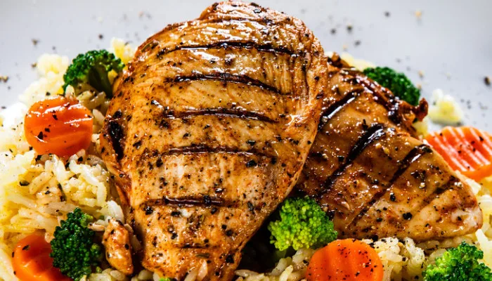 Seasoned grilled chicken breast with grill marks, served with white rice and fresh broccoli and red peppers for foodservice.