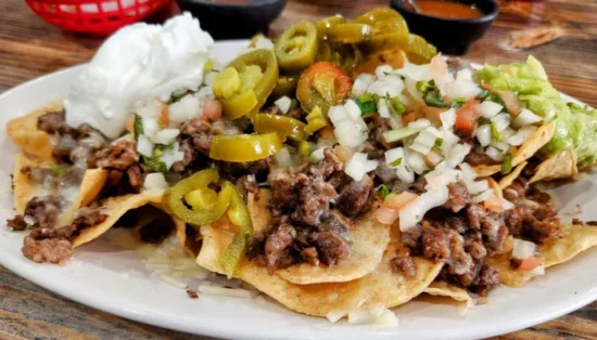 Professional foodservice presentation of crispy tortilla nachos topped with seasoned ground beef, melted cheese, diced onions, tomatoes, jalapeños, and sour cream.
