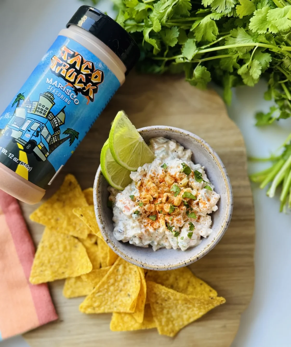 Creamy mango sriracha mayo dip garnished with crispy fried onions and fresh cilantro, served with yellow tortilla chips and lime wedge.
