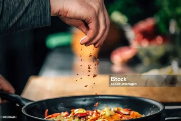 Hand seasoning colorful sautéed vegetables in a lively kitchen pan.