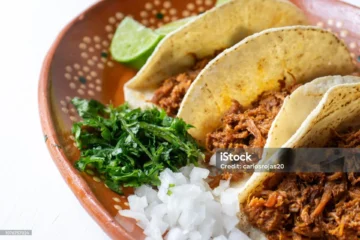 Delicious tacos on a rustic clay plate, garnished with cilantro, onions, and lime wedge.